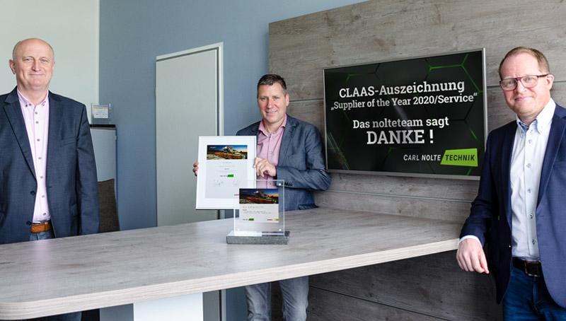 Wir sagen DANKE für die Auszeichnung zum Supplier of the Year 2020 Drei Männer in Anzügen stehen an einem länglichen Stehtisch. Der Mann in der Mitte hält einen Bilderrahmen in der Hand. An der Wand ein Bildschirm mit dem Dankes-Text für die Auszeichnung zum Claas-Lieferanten des Jahres.