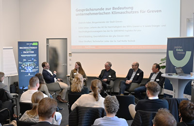 Auf einer Beamerleinwand ist ein Chart der Veranstaltung "Grevener Unternehmensinitiative zum Klimaschutz - Auftaktveranstaltung" dargestellt. Davor 5 Personen in einer Gesprächsrunde, dem Publikum zugewandt